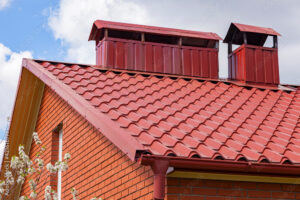 The roof of the house with a chimney.The metal tile is red-brown and the chimney of the heating system on the roof of the house in summer weather.