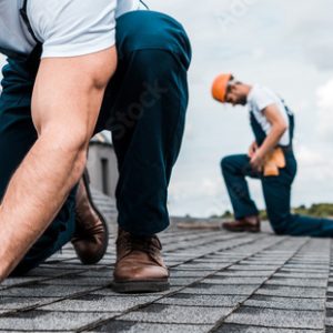 panoramic shot of handyman holding hammer while repairing roof near coworker